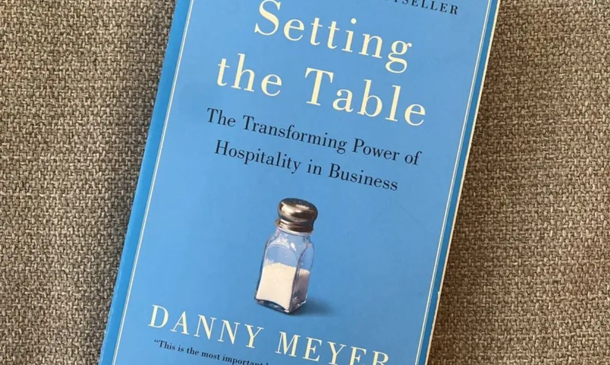 Cover of Danny Meyer's book Setting the Table: The Transforming Power of Hospitality in Business, lying on a woven fabric surface with a small salt shaker pictured on the cover